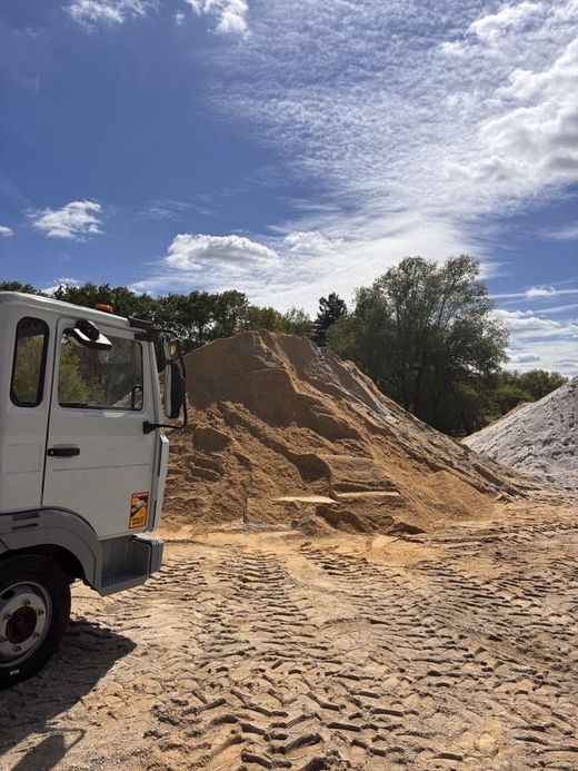 Un camion blanc garé à côté d'un grand tas de sable sur un chantier de construction ou une carrière.