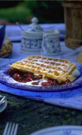 Eine Waffel mit Erdbeeren und Schlagsahne auf einem blauen Teller auf einem Tisch.