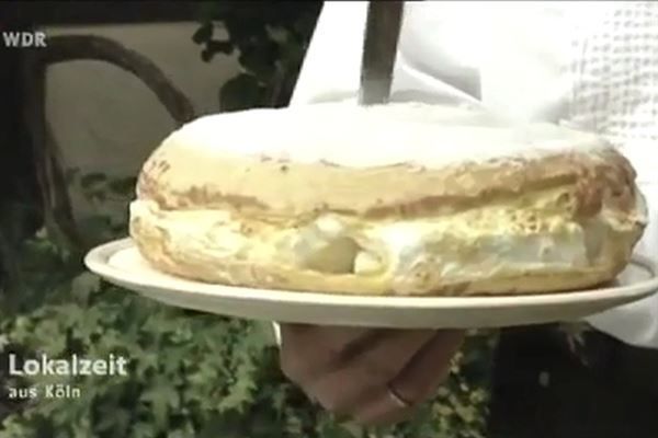 Eine Person hält einen weißen Teller mit einem Kuchen darauf.