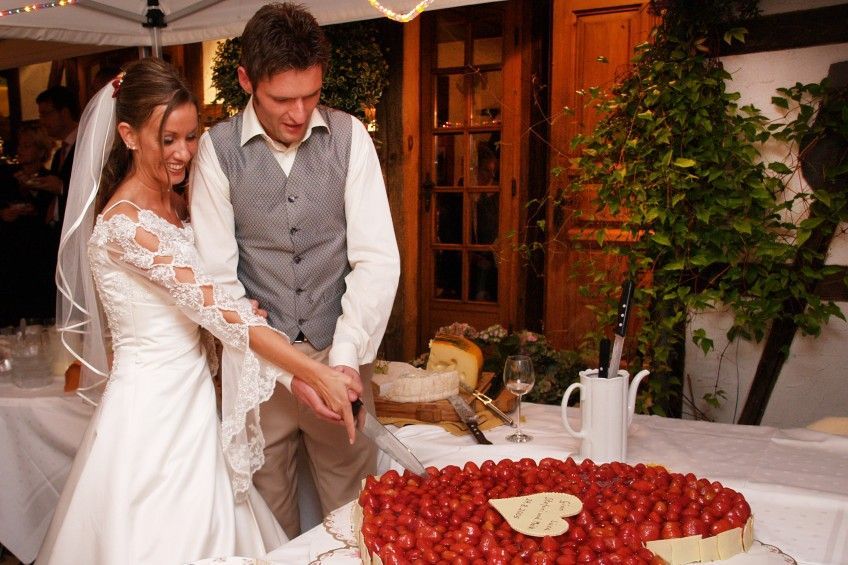 Braut und Bräutigam schneiden einen Kuchen mit Erdbeeren darauf an