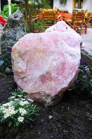 Ein großer rosafarbener Felsen liegt inmitten eines von Blumen umgebenen Gartens.