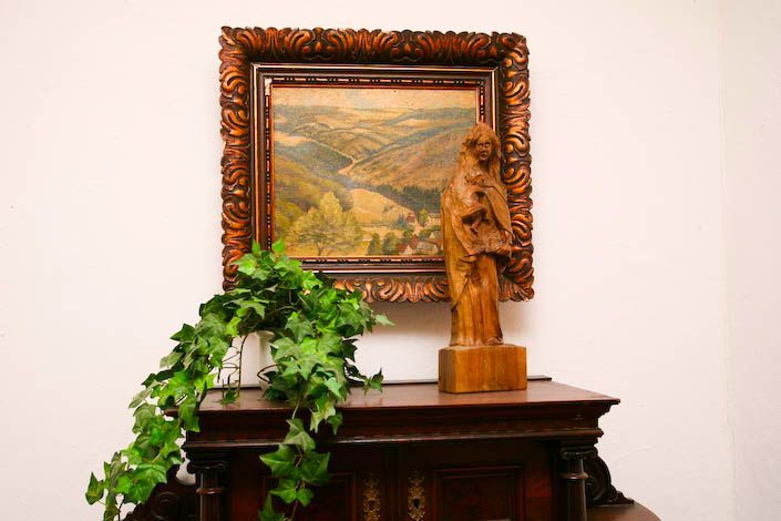 Eine Holzstatue sitzt auf einer Kommode unter einem Gemälde