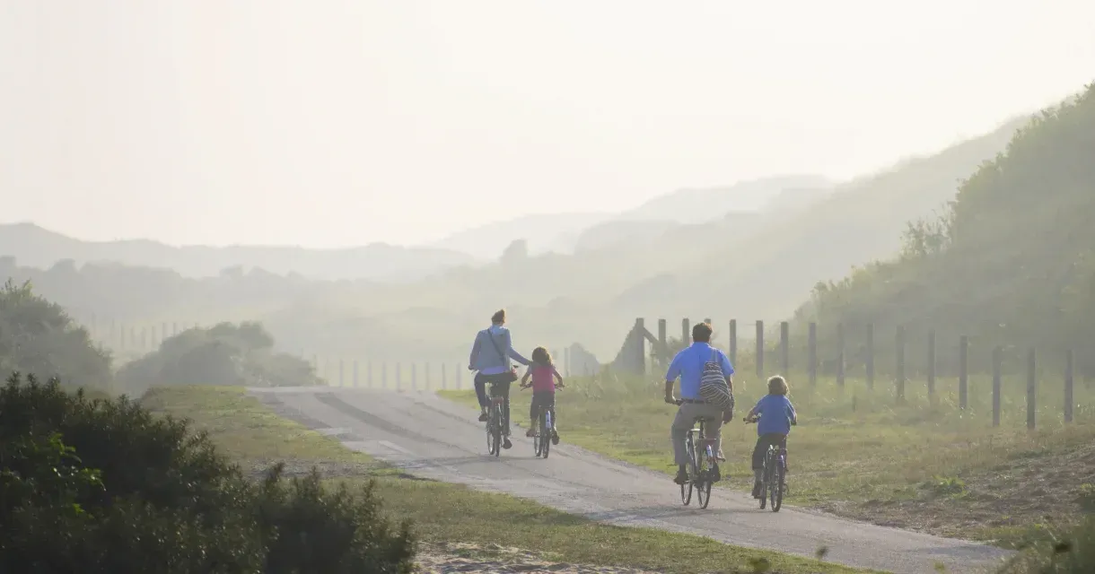 Fietsers en een kind rijden over een mistige landweg langs velden en heuvels.