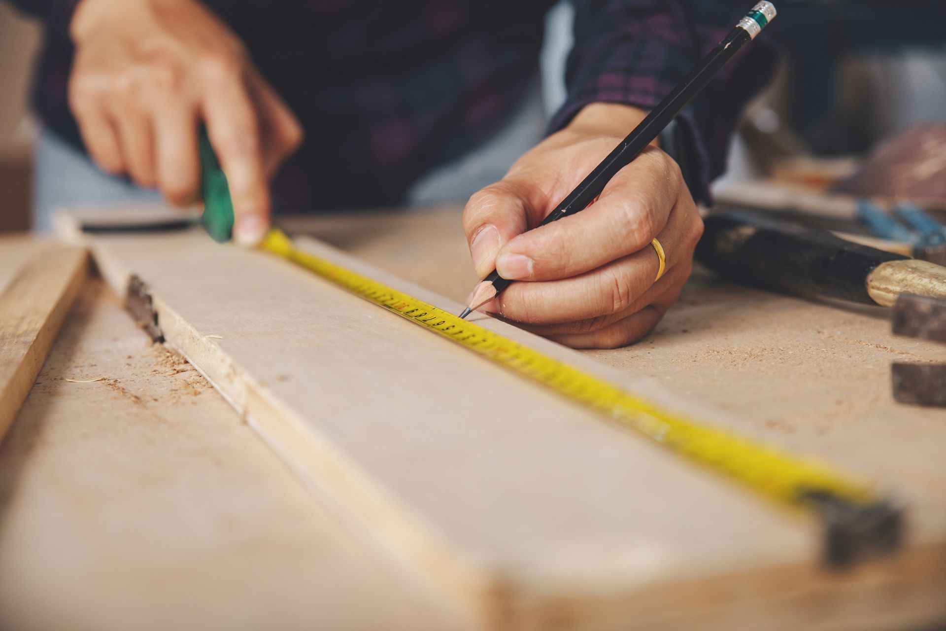 Une personne mesure un morceau de bois avec un ruban à mesurer et un crayon.