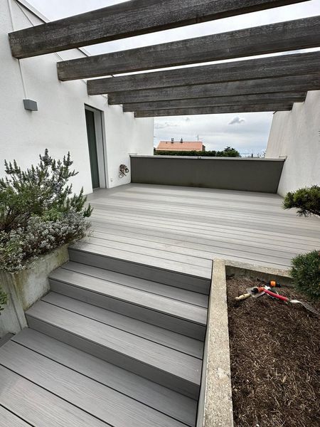 Une terrasse en bois avec des escaliers qui y mènent et une pergola.