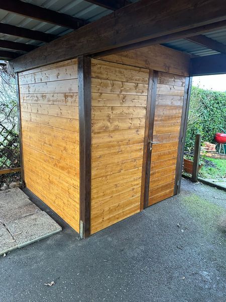 Un hangar en bois avec deux portes se trouve sous un abri d'auto.