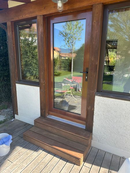Une porte en bois avec une fenêtre en verre est posée sur une terrasse en bois.