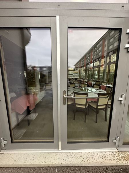 Un restaurant avec des tables et des chaises se reflète dans une porte vitrée.