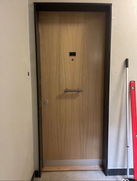 Une porte en bois dans un couloir à côté d'une serpillère rouge.