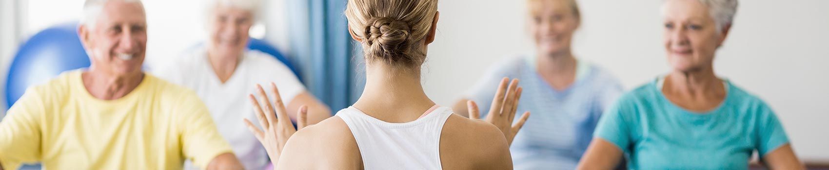 Eine Frau bringt einer Gruppe älterer Menschen Yoga bei.