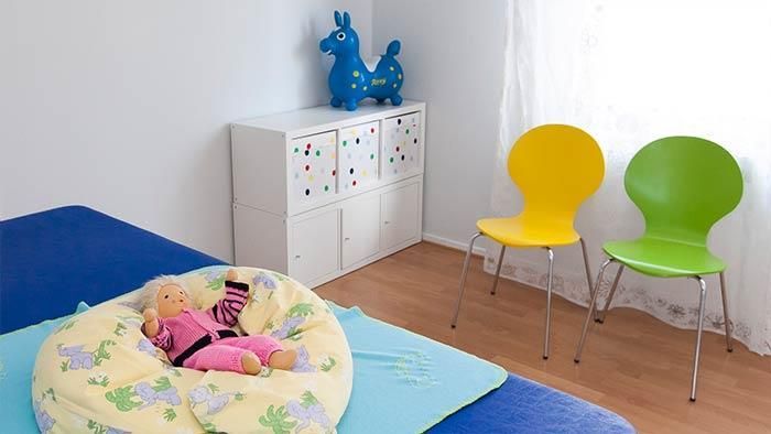 Ein Baby sitzt auf einem Kissen in einem Raum mit Stühlen