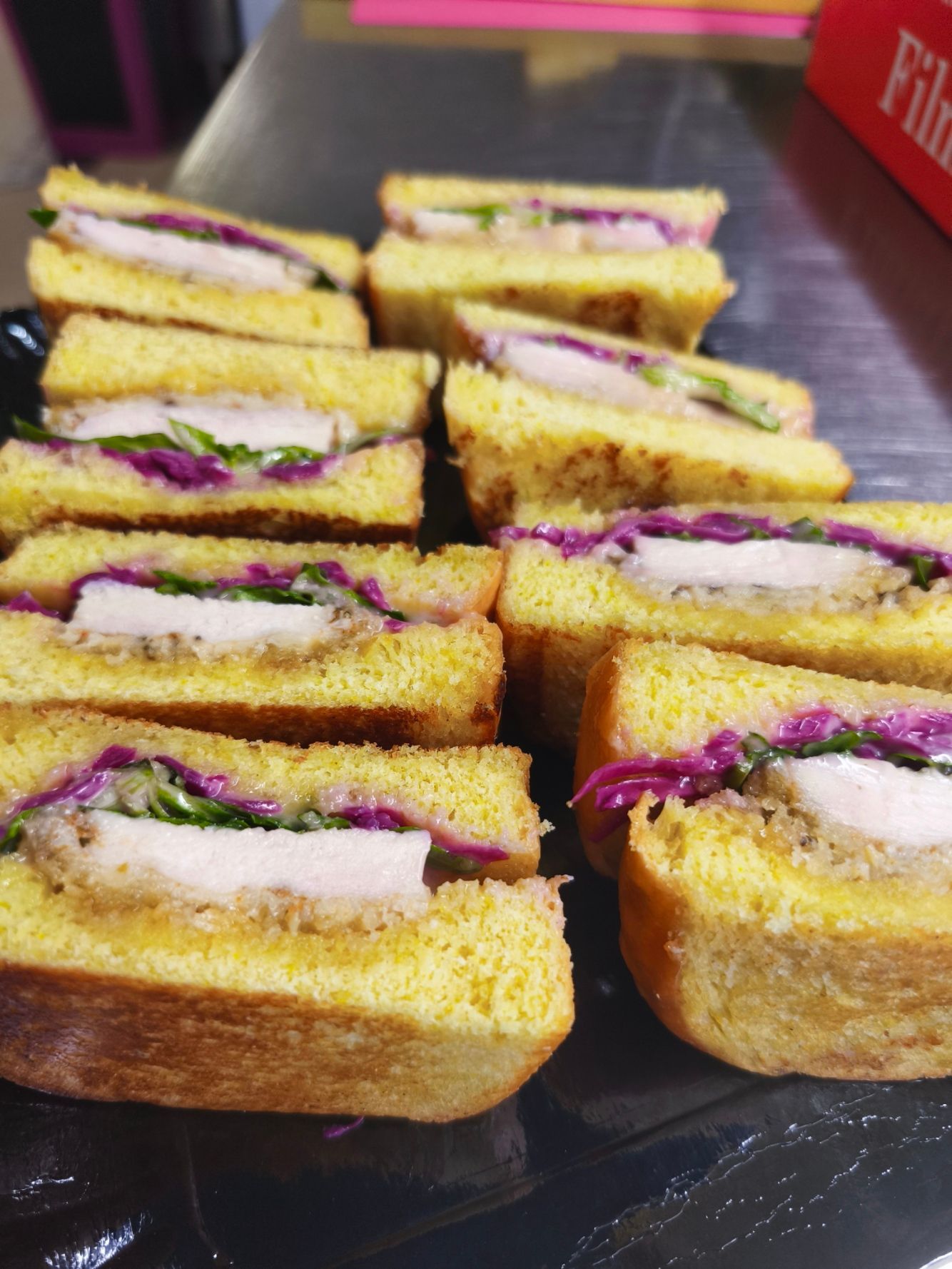 Un plateau de gaufres rectangulaires en amuse-bouche, garnies de crème fouettée, de tranches de fruits et de morceaux de cornichons.