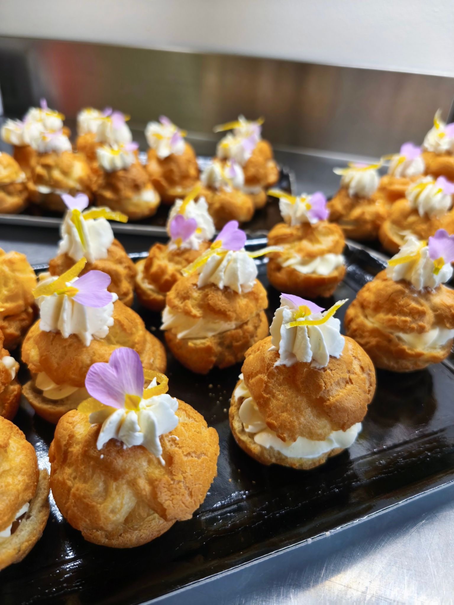 Gâteau en forme de lettre E décoré de glaçage, de fleurs en sucre roses et de bonbons au chocolat assortis, présenté sur un plateau foncé.