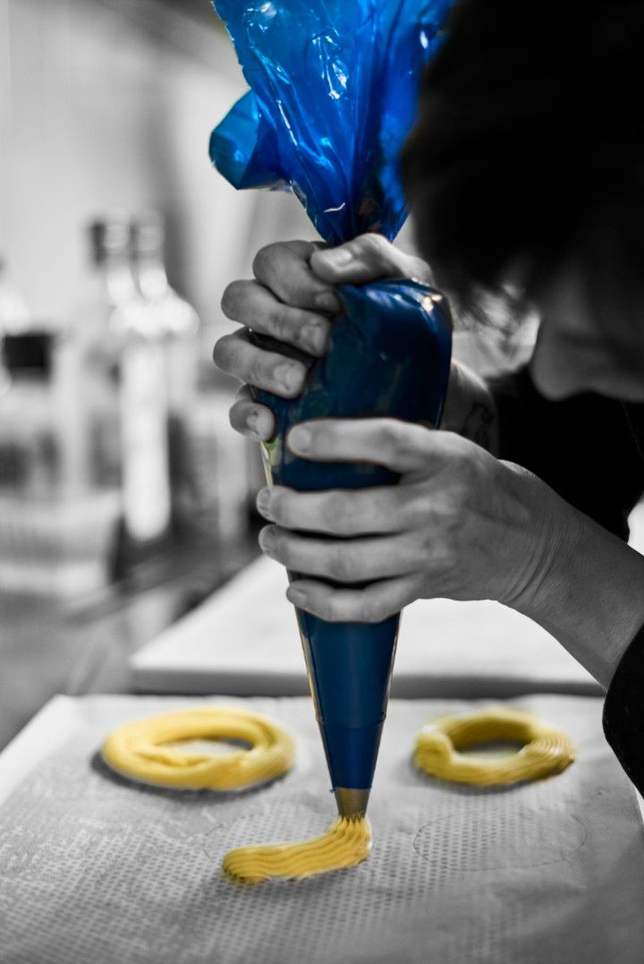 Une personne utilise une spatule jaune pour portionner la pâte sur une surface sombre, près d'une rangée de moules à pâtisserie en métal.