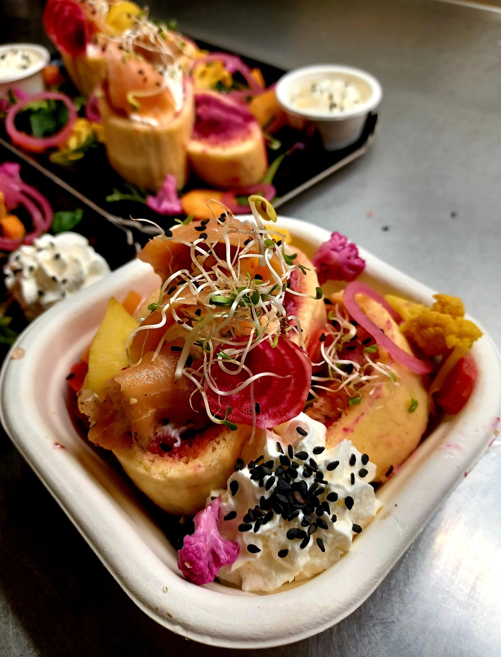 Deux bols carrés de saumon coloré, de betteraves tranchées, de germes et de fromage à la crème, garnis de graines de sésame noir.