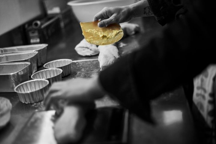 Dans une cuisine professionnelle, un boulanger travaille la pâte, tenant une spatule à pâte jaune au-dessus d'un plateau de moules métalliques.