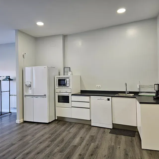 Una cocina con gabinetes blancos, un refrigerador, un microondas y un fregadero.