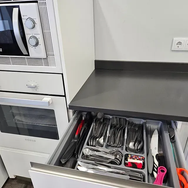 Una cocina con un horno microondas y un cajón lleno de utensilios.