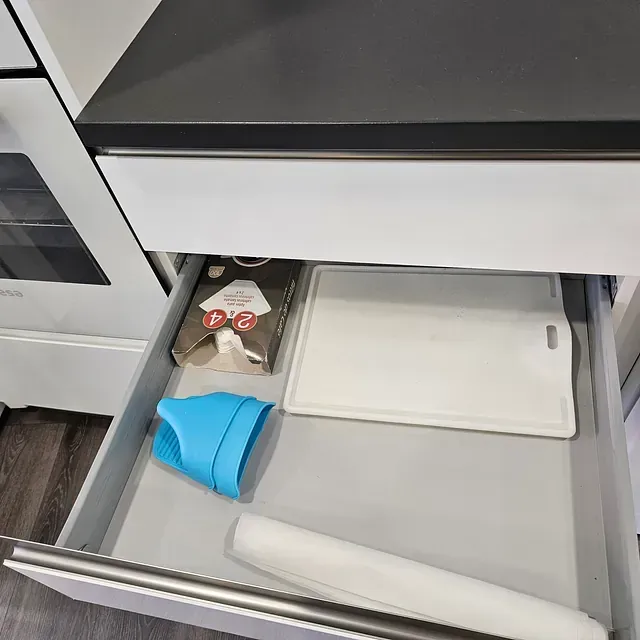 Un cajón de cocina con una tabla de cortar y un rodillo dentro.