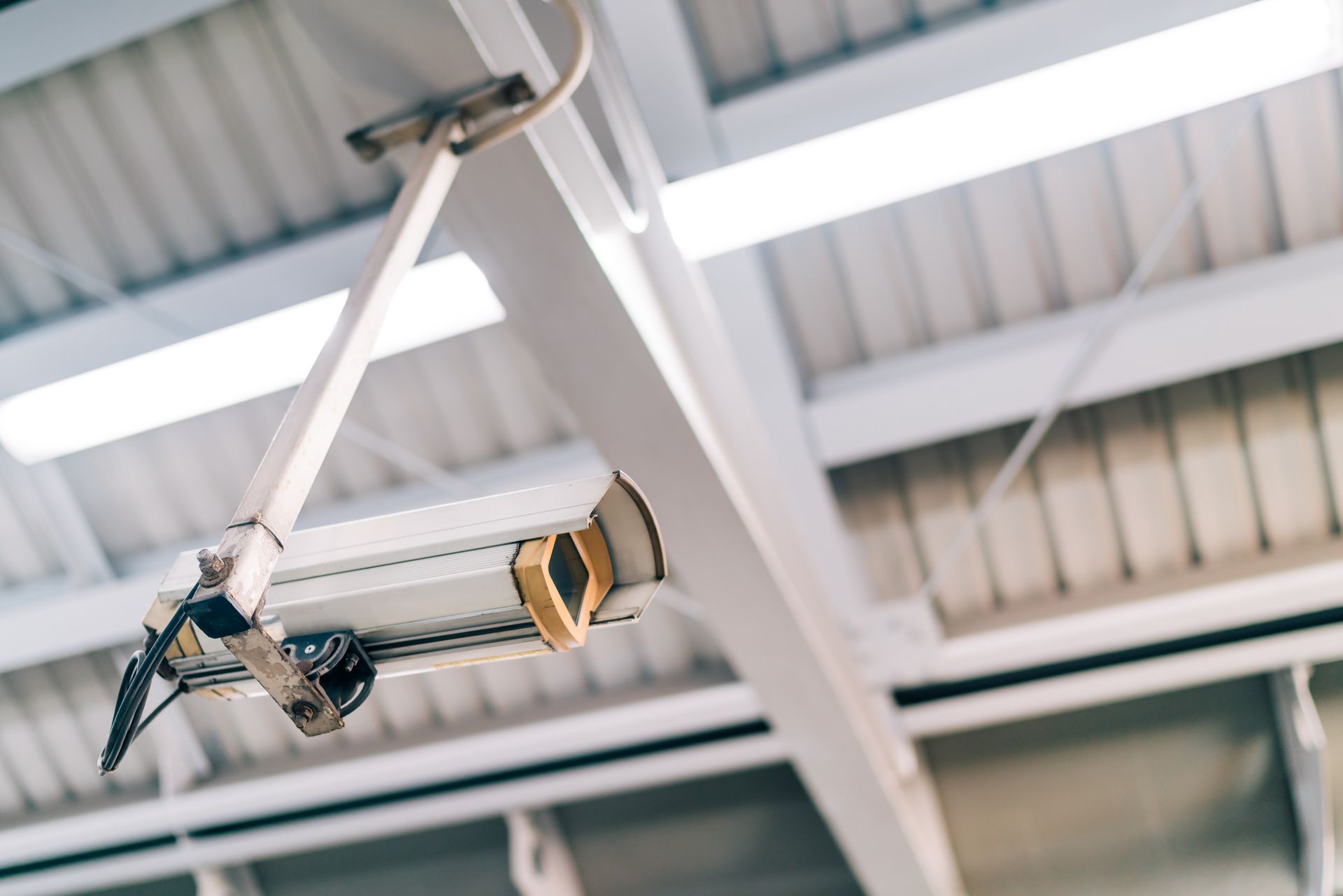Cámara de seguridad montada en un techo industrial blanco, en ángulo hacia abajo.