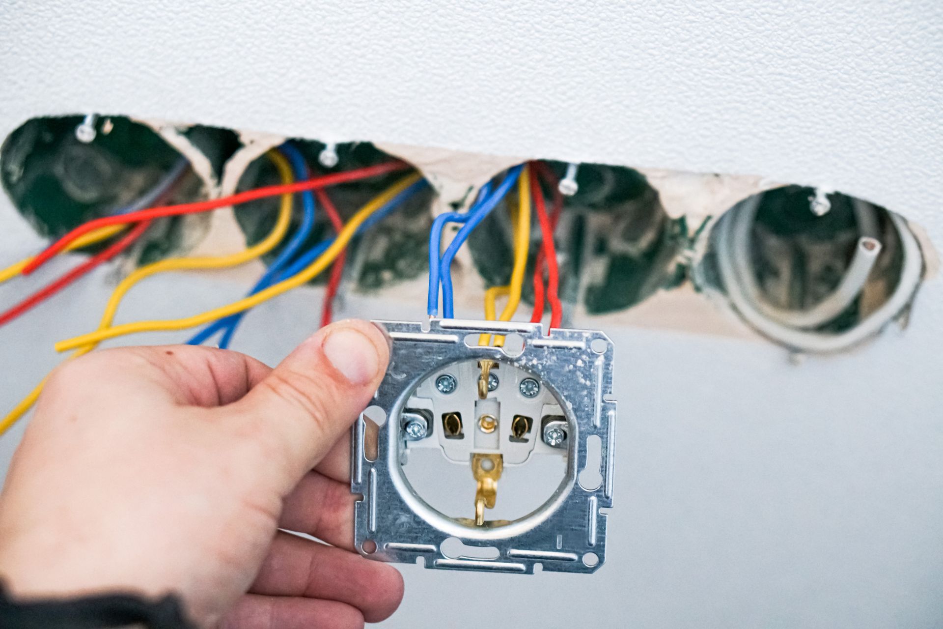 Mano sosteniendo una toma de corriente eléctrica europea, cables expuestos en la pared, lista para la instalación.