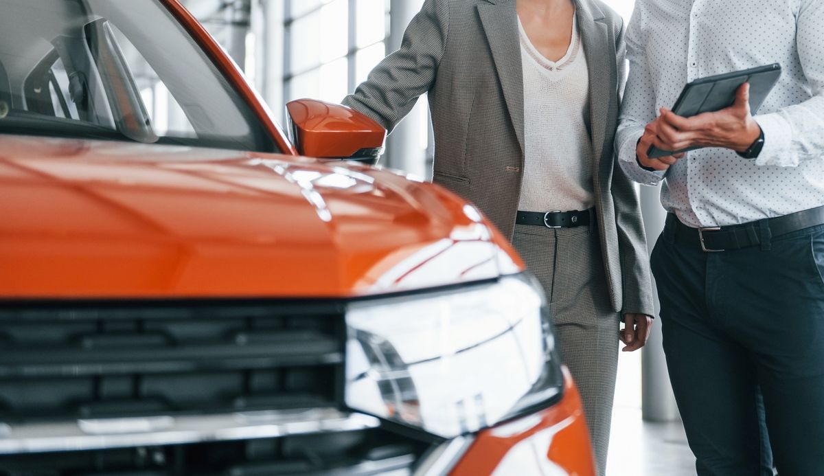 Dos personas conversan sobre un coche de color naranja brillante en una sala de exposición mientras sostienen una tableta.
