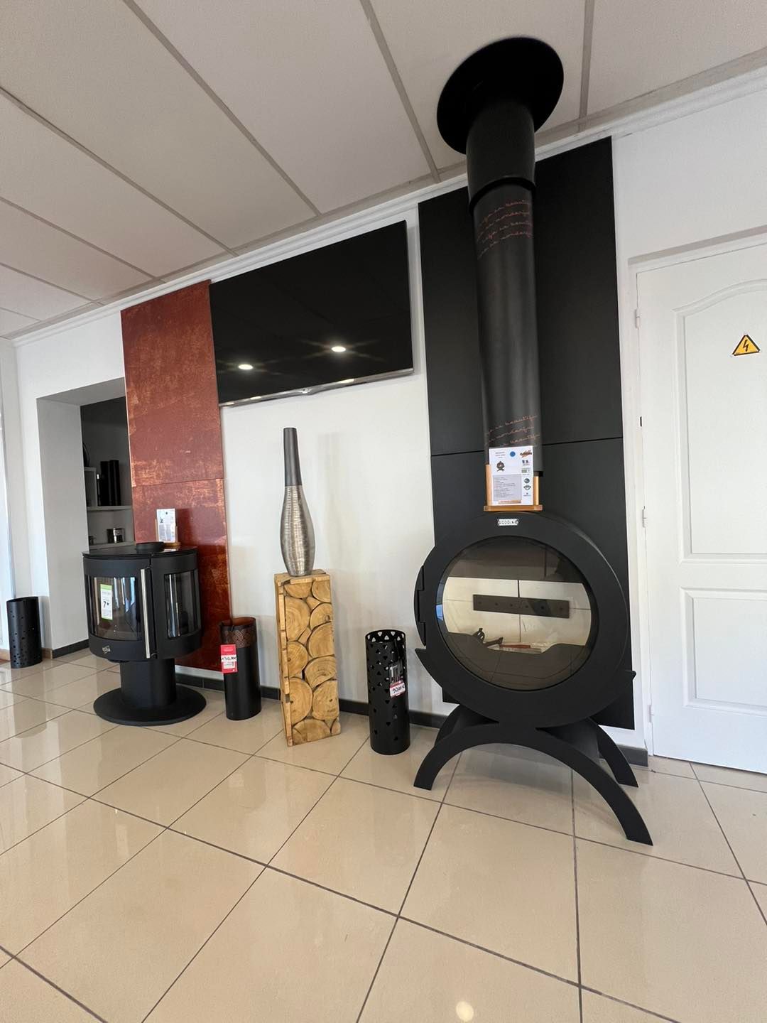 Une salle d'exposition présentant diverses cheminées noires, dont un modèle circulaire avec conduit, disposées sur un sol carrelé.