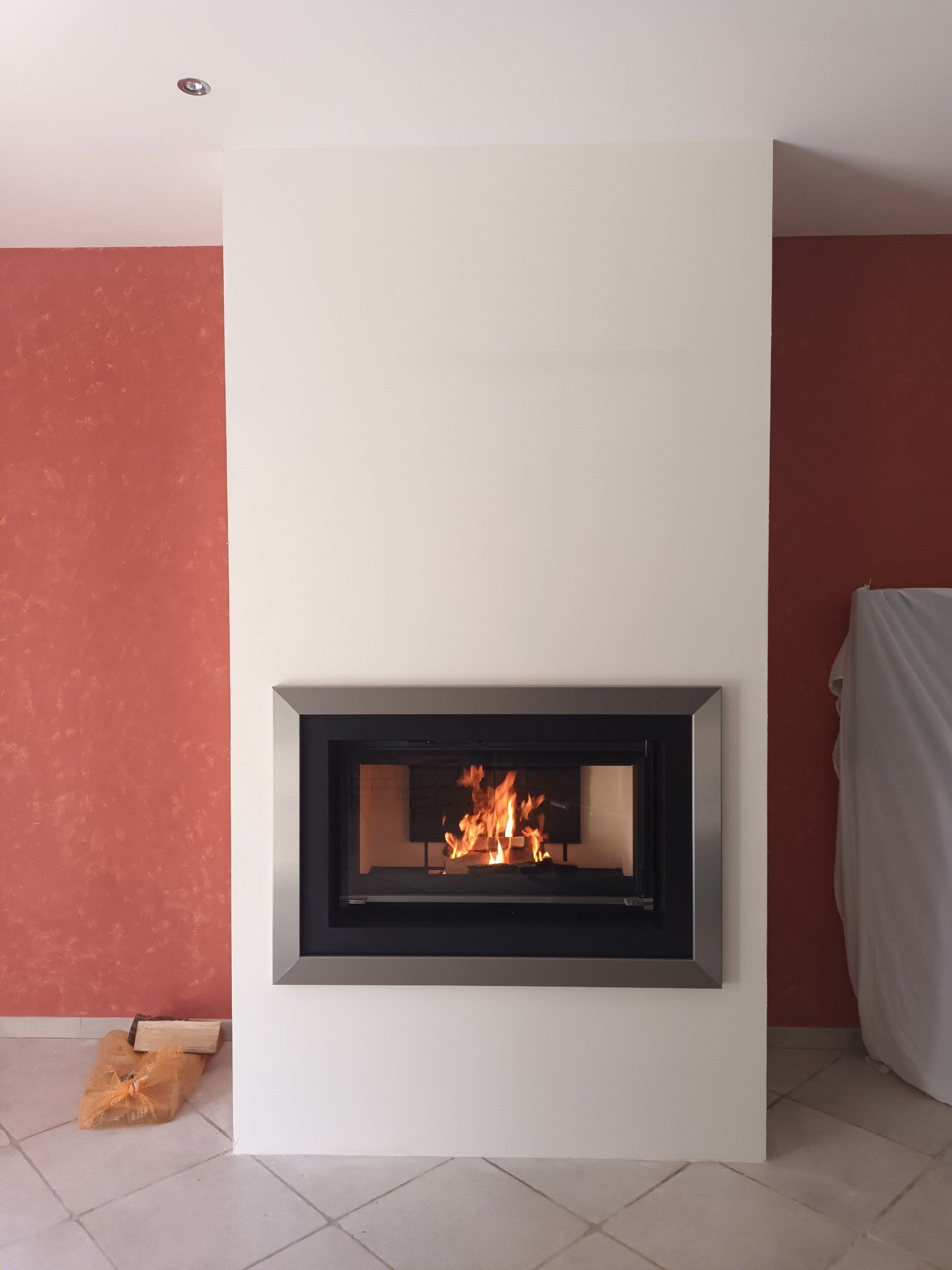 Cheminée avec flammes dans un encadrement blanc moderne, sur fond de murs rouges.