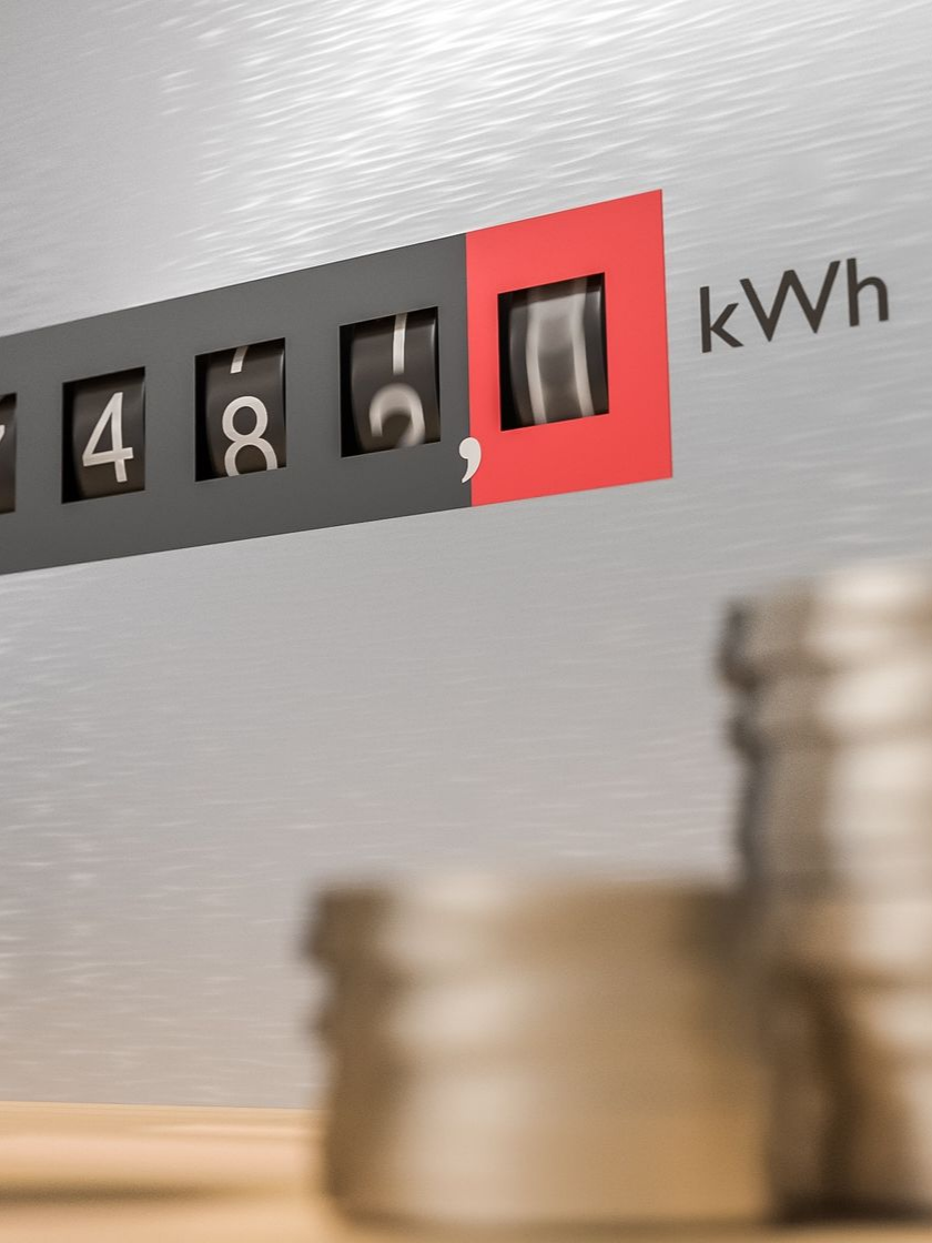 Gros plan sur un compteur d'énergie affichant 7 482 kilowattheures, avec des pièces de monnaie floues au premier plan.