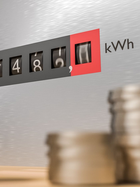 Gros plan sur un compteur d'énergie affichant 7 482 kilowattheures, avec des pièces de monnaie floues au premier plan.