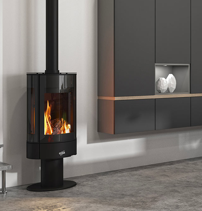 Cheminée moderne noire avec flammes, tuyau noir, à côté de meubles gris, sol en béton.