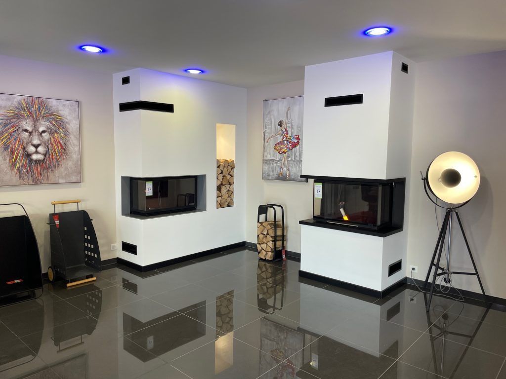 Salle d'exposition de cheminées modernes avec murs blancs, sol réfléchissant et œuvres d'art.