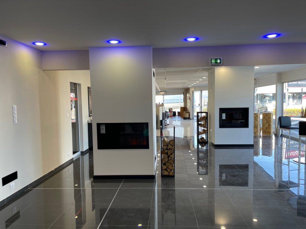 Intérieur de showroom moderne avec cheminées, sol brillant et éclairage bleu au plafond.