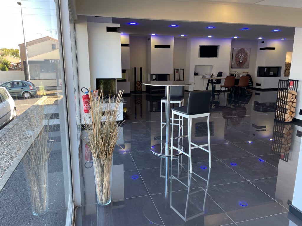 Intérieur de la salle d'exposition avec cheminées, tabourets de bar et sol poli reflétant l'espace.