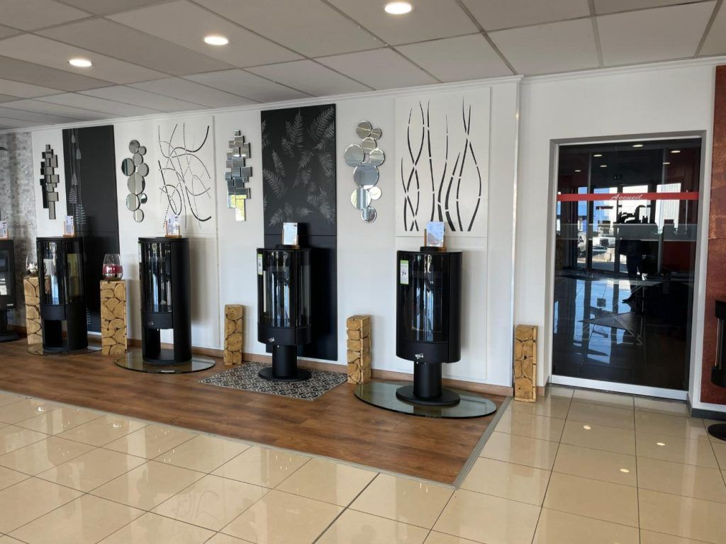 Une salle d'exposition avec des poêles noirs devant des panneaux décoratifs et une porte.