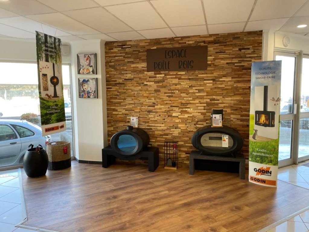 Salle d'exposition de poêles avec sol imitation bois, mur en pierre et plusieurs poêles à bois noirs exposés. La lumière du soleil y pénètre abondamment.