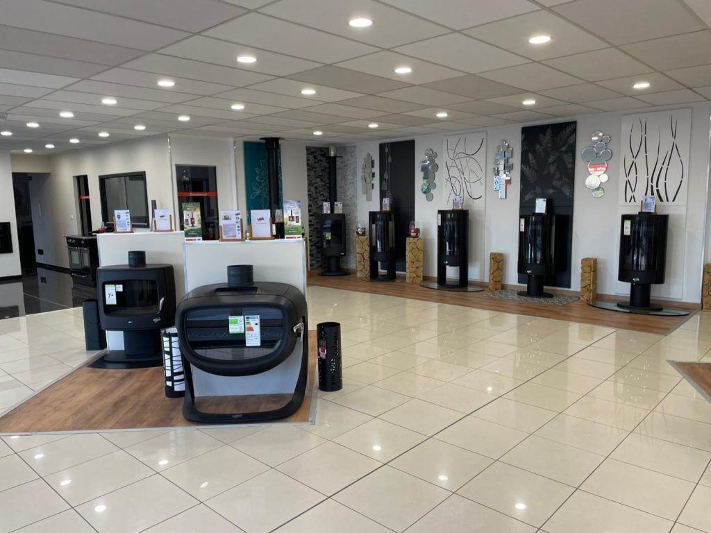 Intérieur d'une salle d'exposition présentant divers poêles à bois noirs et des panneaux muraux décoratifs.