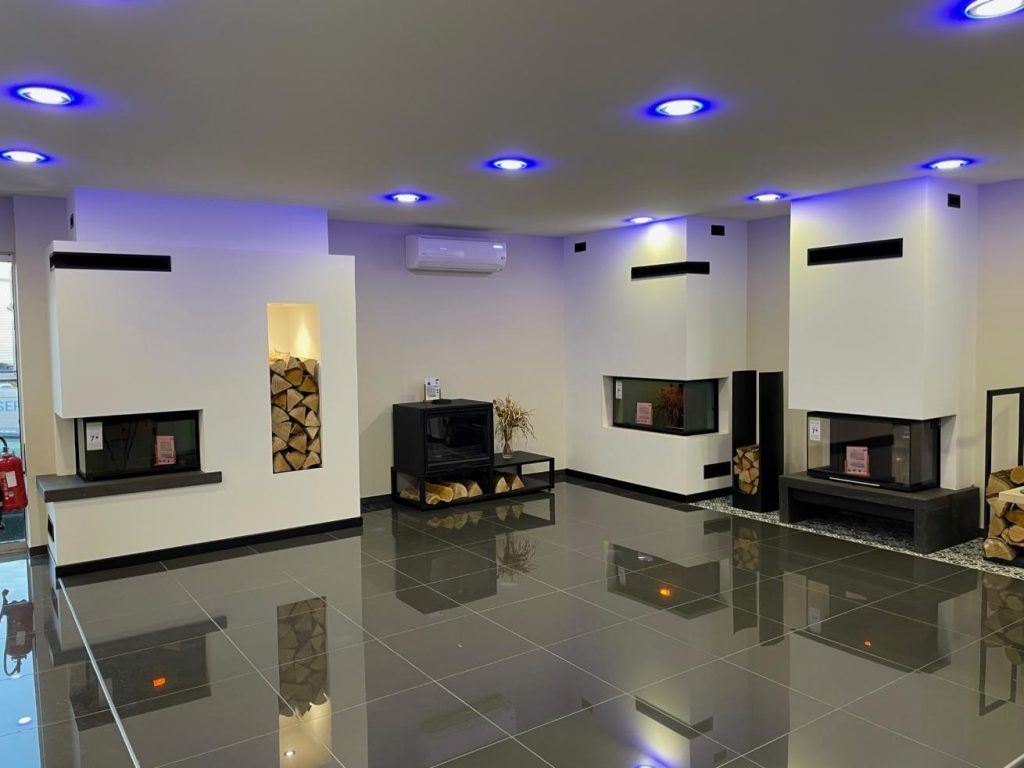 Showroom moderne avec cheminées et rangements à bois, se reflétant dans les sols noirs brillants. Éclairage bleu au plafond.