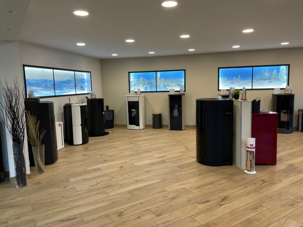 Salle d'exposition présentant plusieurs poêles modernes, avec parquet et œuvres d'art rétroéclairées représentant des scènes d'hiver.