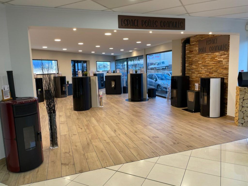 Salle d'exposition présentant différents poêles à bois cylindriques sur un sol imitation bois, avec un mur d'accent en briques.