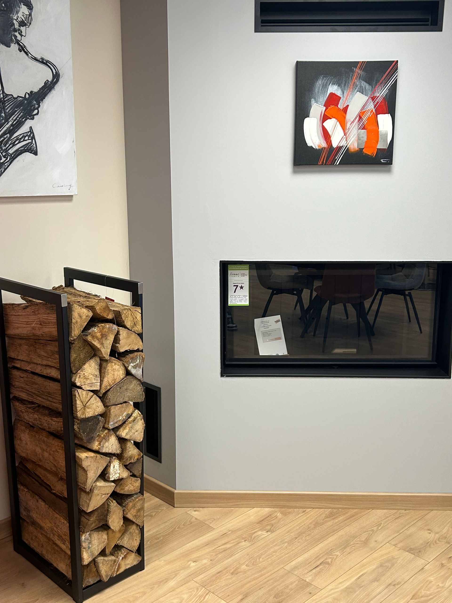 Intérieur d'une salle d'exposition présentant divers foyers et poêles, avec de grandes fenêtres donnant sur un parking.