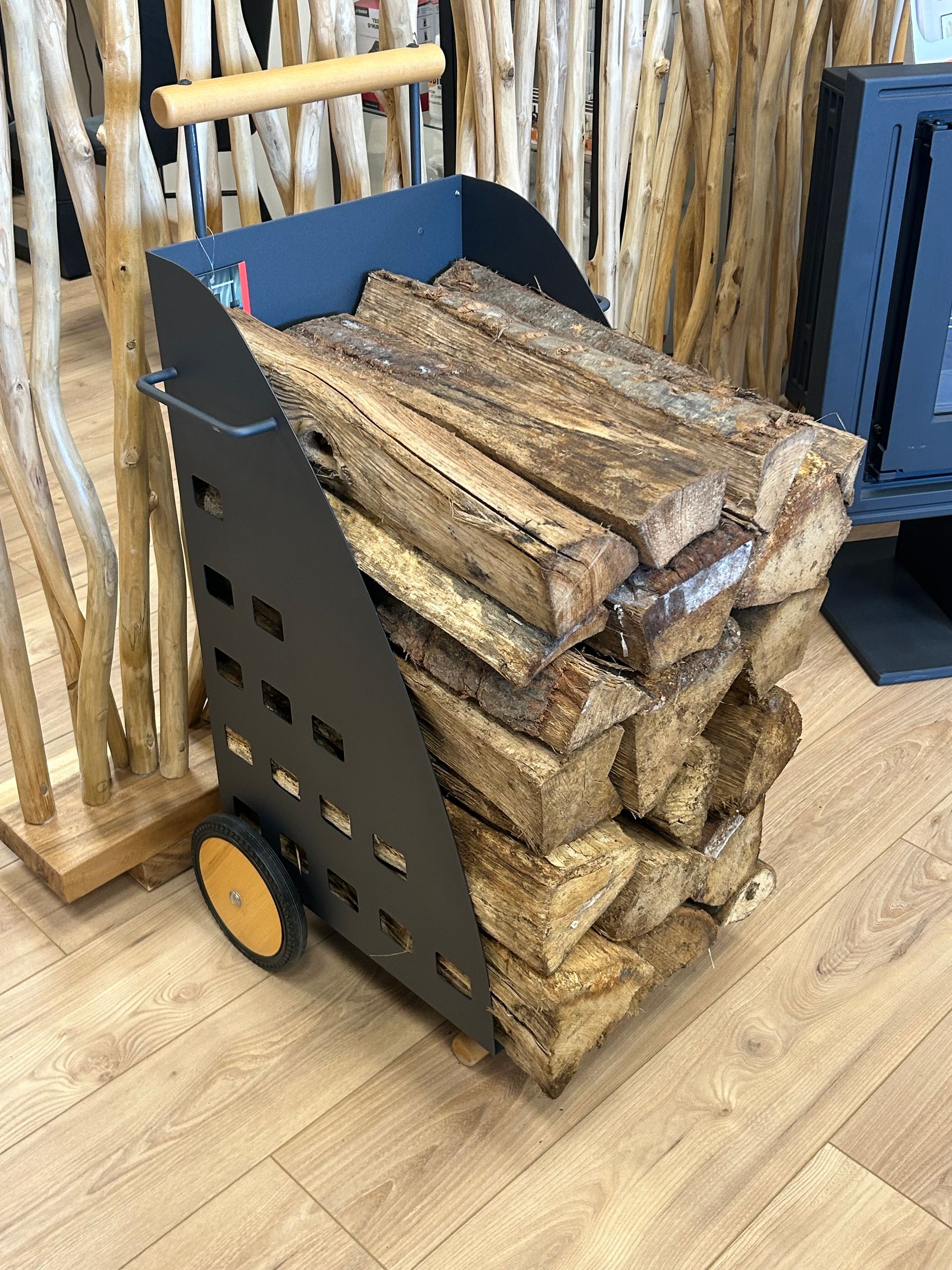 Caddie de bûches en métal noir avec poignée en bois et roues.