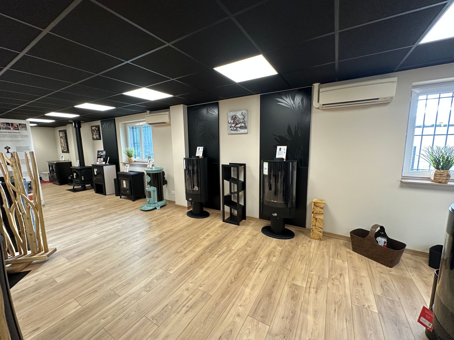 Une salle d'exposition avec plusieurs poêles à granulés et un purificateur d'air sur un parquet, avec une œuvre d'art représentant un paysage d'hiver au-dessus.