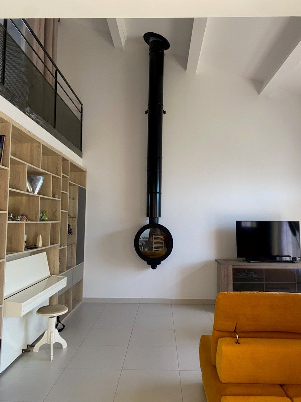 Salon moderne avec poêle suspendu, piano et canapé jaune.
