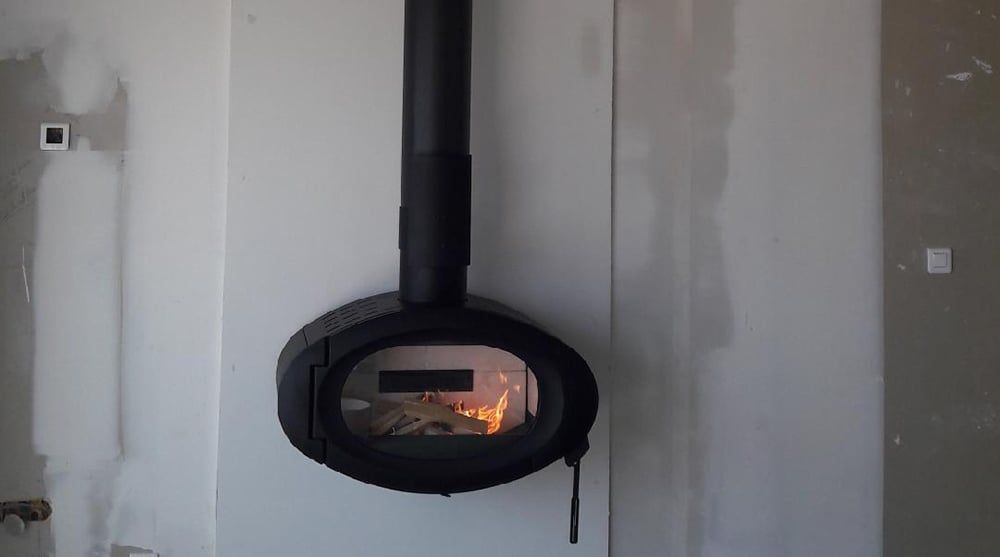 Poêle ovale noir avec des flammes ardentes et un conduit de cheminée noir sur un mur blanc.