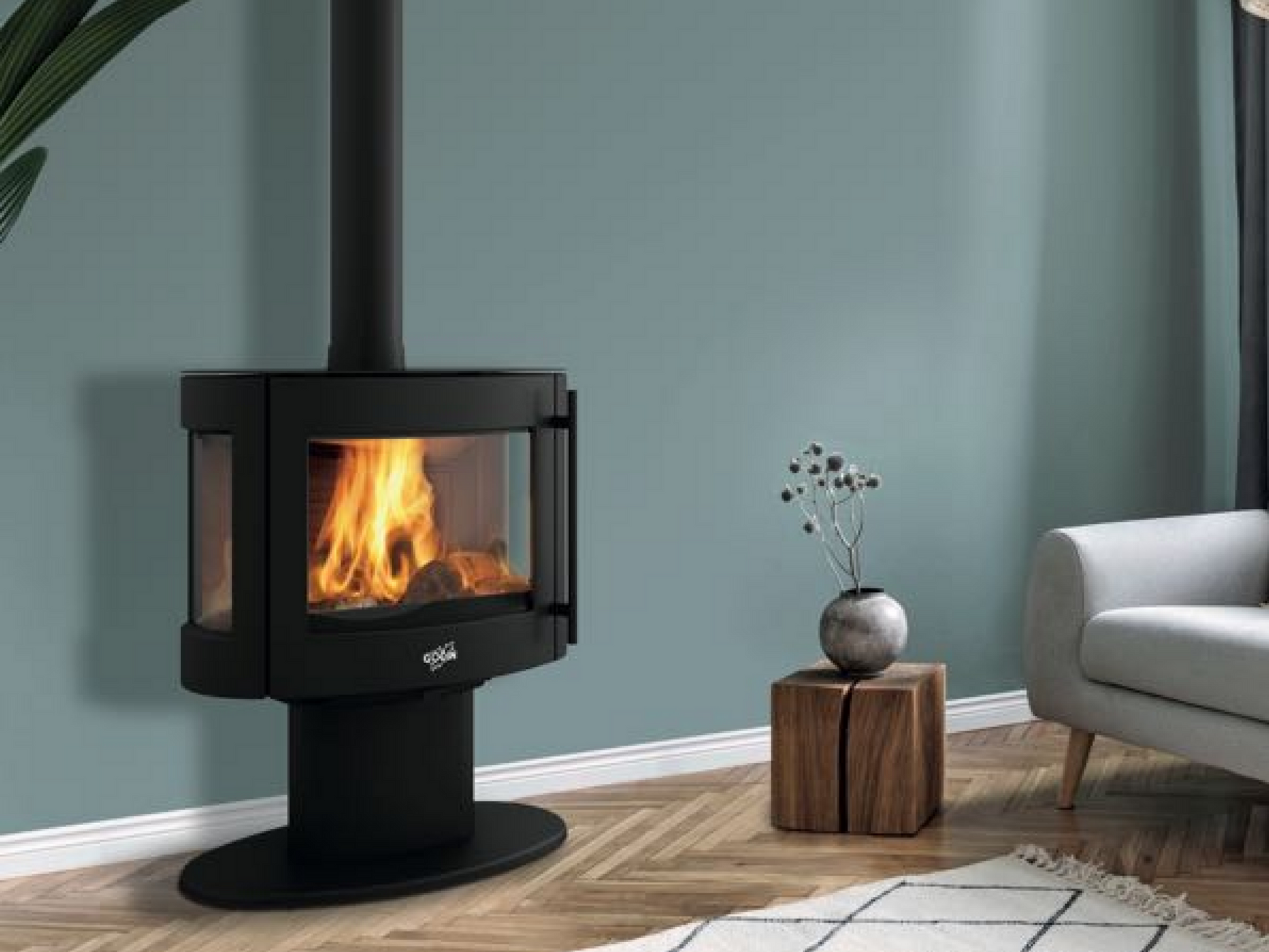 Cheminée noire avec des flammes sur un mur turquoise. Table d'appoint en bois, canapé gris et tapis.
