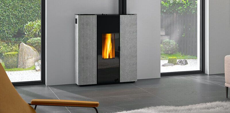 Un poêle à granulés moderne avec une flamme allumée, dans une pièce dotée de grandes fenêtres donnant sur un jardin.