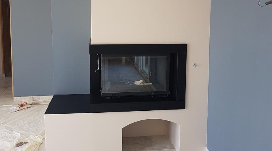 Cheminée à cadre noir et porte vitrée, installée dans une alcôve beige clair, sur fond de murs gris.