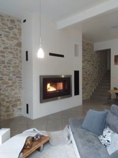 Cheminée moderne encastrée dans un mur blanc avec des accents de pierre, un intérieur éclairé et un luminaire.