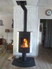 Poêle à bois moderne avec flammes, tuyau noir et fond mural blanc.